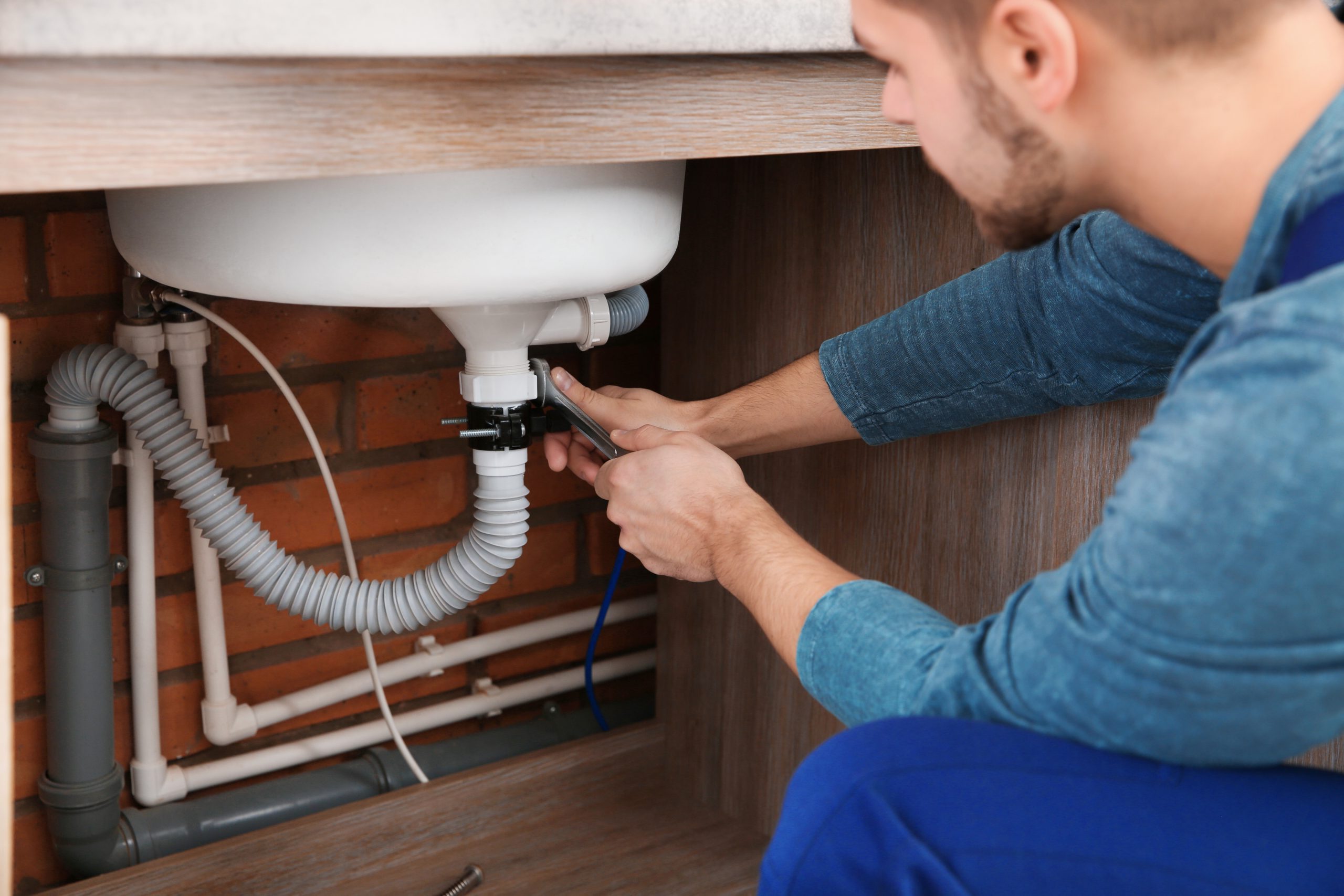 Male plumber in uniform repairing kitchen sink