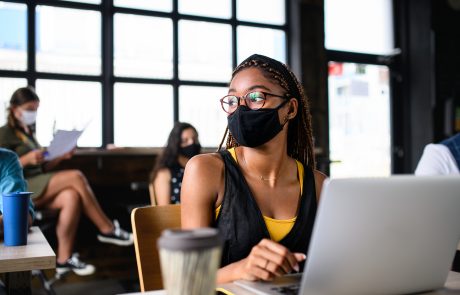 Portrait of young businesswoman with face mask working indoors in office.