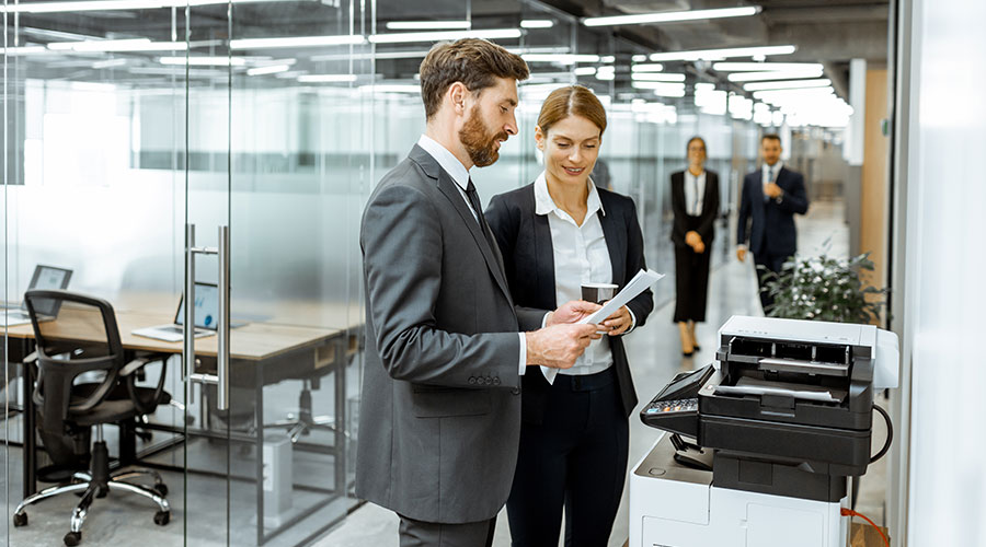 Two co-workers using a printer in office environment