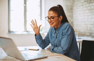 A woman waving at her colleagues through a video conference