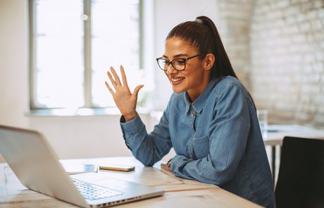 A woman waving at her colleagues through a video conference