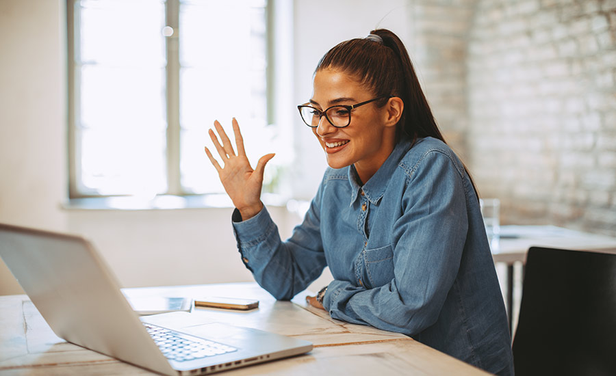 A woman waving at her colleagues through a video conference