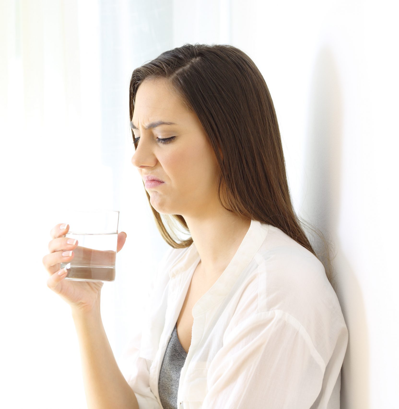 Disgusted woman drinking water with bad taste on white